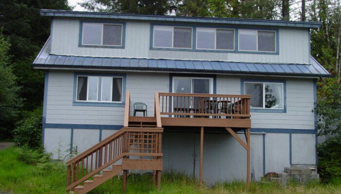 Blue two-story house with wooded background